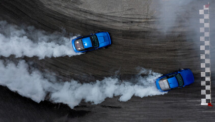Aerial top view two cars drifting battle on asphalt race track with lots of smoke from burning tires, Two race cars competition drift battle view from above. © Kalyakan