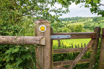 A yellow waymark arrow showing a public footpath on the Cotswolds near Nashend, Gloucestershire, England UK
