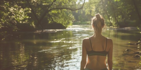 Fototapeta premium Woman enjoying nature by the river. Young woman standing in a serene river environment, enjoying nature and the tranquility of the peaceful surroundings. Banner with copy space