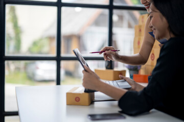 Two women are sitting at a table with a laptop and a pen