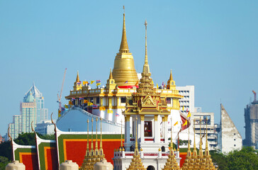 Naklejka premium Stunning Phu Khao Thong (Golden Mount) of Wat Saket Temple with the Spires of Loha Prasat (Iron Castle) of Wat Ratchanatdaram Temple in Foreground, Bangkok City Skyline, Thailand