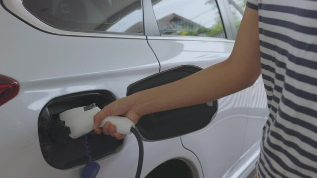 Woman charging her electric vehicle (EV) while using her mobile phone to control the process. It shows the convenience and efficiency of smart charging systems and integration of modern technology. 