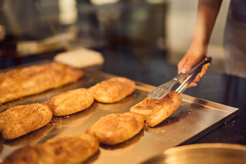 A female baker is catching a fresh pastry from a glass case.