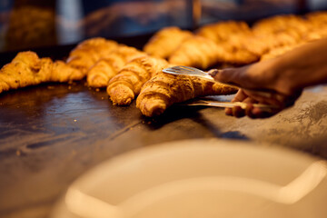 A seller using kitchen tongs, holding a freshly baked croissant.