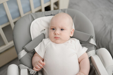 Cute baby is awake on high chair, baby lounger, and spends his time actively. Portrait of newborn baby. Concept of child care, happy childhood. Goods for children