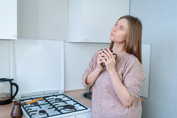 A woman is standing in a kitchen with a cup in her hand