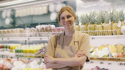 In front of a vibrant produce display, a cheerful supermarket employee stands confidently, ready to assist customers with a smile in this bustling grocery store environment