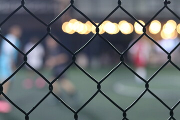 Fototapeta premium Mini soccer field with fence and blurred players in the background, selective focus 
