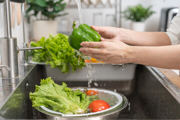 Close up hand of asian young housekeeper woman, washing sweet pepper, green paprika, vegetables with splash water in basin of water on sink in kitchen, preparing fresh salad, cooking meal. Health food