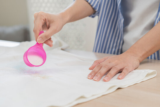 Dirty stain concept, asian young housewife woman removing spill from white T-shirt hand holding stain remover bleach spoon to remove dirt stain, stains on clothes, dirty spot for washing and cleaning.