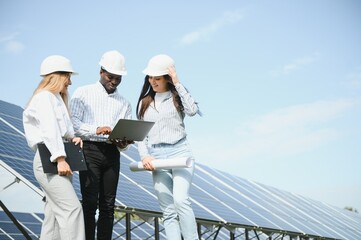 Group of multi ethnic people and safety helmets staring at solar farm.