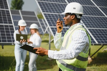 Construction site African worker wearing safety vest and helmet holding a radio, solar panel