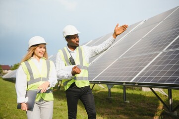 Multiracial people having working discussion about green energy while standing outdoors. Solar panels arranged around.