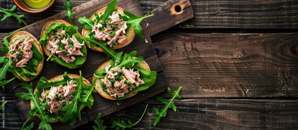 Poster top-view image of canned tuna toasts or sandwiches with lettuce and arugula on a dark wooden backdro