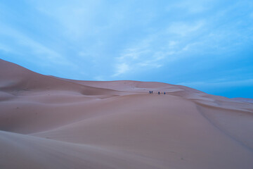 Gentle waves of sand dunes under a pastel sunrise sky. A moment of peace in Merzouga, Morocco.