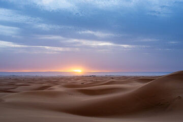 Gentle waves of sand dunes under a pastel sunrise sky. A moment of peace in Merzouga, Morocco.