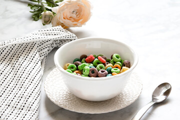 Morning breakfast scene of colorful cereal in a white bowl on a white plate with a white backdrop. A table napkin, spoon, and a flower on the side