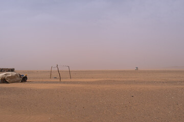 A car speeds across the sandy plains of Merzouga during a dust storm; visibility is reduced to a haze. Temporary shelter in view, Morocco.
