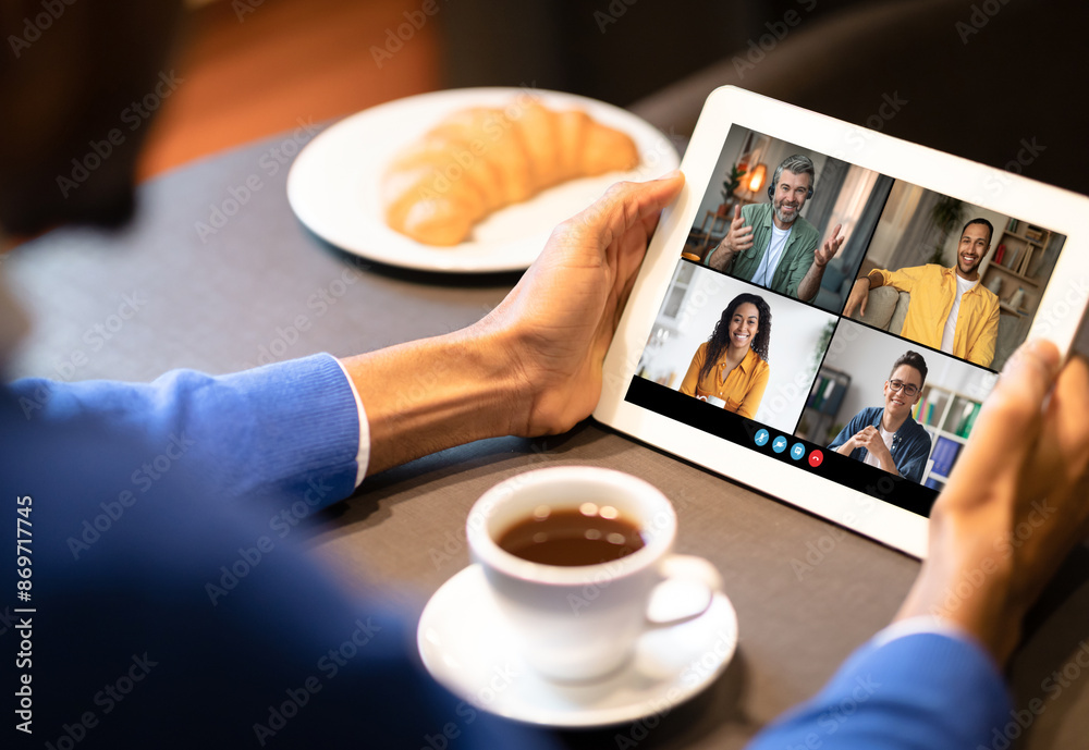 Poster black man sits at a table in a casual setting, participating in a video conference on a tablet. the 