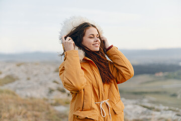 Alone traveler in yellow coat standing on hill with hands on ears in a peaceful moment