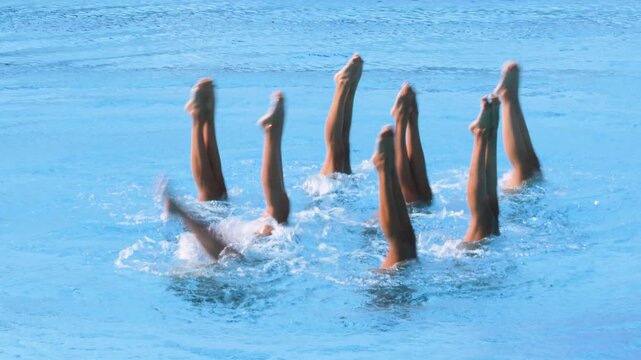 Artistic swimmers team performing synchronized choreographed legs movement in the swimming pool