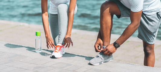 Couple Activities And Jogging. Black Man And Woman Lacing Their Shoes Next To River Embankment. Cropped, Panorama, Copy Space
