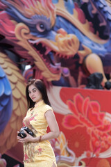 A pretty woman in yellow chinese traditional costume holding a vintage film camera in front of colorful dragon background. The Chinese new year celebration.