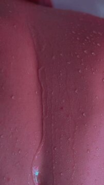 handsome young man washes himself under a cold shower in the bathroom. Drops of water flow down the skin and perfect skin of a man close up