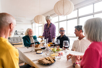 Group of happy senior friends bonding at home for dinner party - Cheerful and youthful old mature multiethnic people having fun