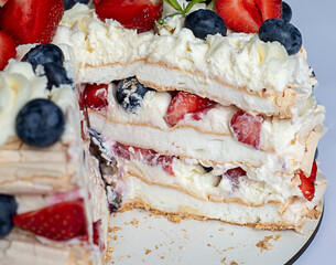 Meringue cake with cream, strawberry and blueberry filling, cut out piece