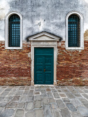 A small church front with green door and windows by a  Venetian street. Travel to Venice, Italy.