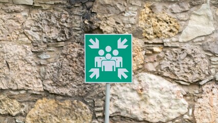 Green Assembly Point Sign on Stone Wall
