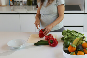Cropped shot of a pregnant woman on a third trimester cooking a healthy plant based meal on a white marble countertop. Close up, copy space, background.