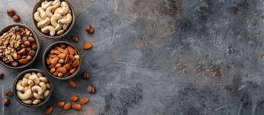 Poster Flat lay of various nuts like hazelnuts, cashews, and almonds in bowls on a textured background with copy space image.