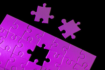 A puzzle with a missing piece and two pieces of the puzzle on the ground. The puzzle is purple and the mood of the image is somewhat sad or incomplete