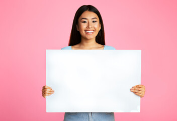 Asian young woman with long black hair is standing in front of a pink background. She is holding a...