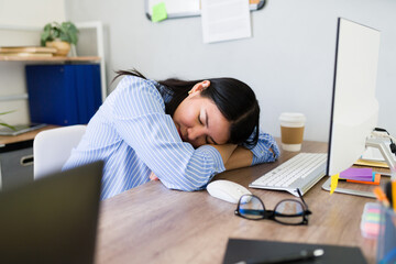 Exhausted young woman takes a power nap at her messy desk, illustrating the toll of a hectic workday