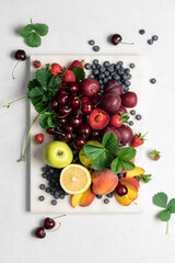 Set of summer ripe berries and fruits on a marble board, top view with copy space. Cherry, strawberry, blueberry, apples, lemon, plum, peach on a light background