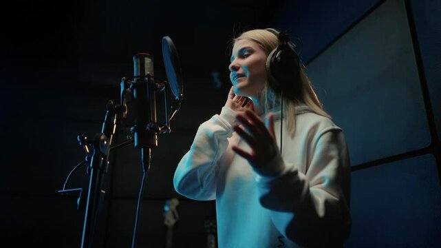 Modern sound studio for recording music, portrait of singing woman singer. Record of soundtrack, musical album or voice acting, young adult lady performing rap song, gesticulating actively by hands