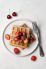 Belgian waffles sprinkled with powdered sugar with strawberries and cherries top view on a white background with copy space