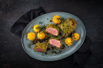 Fried mangalica pork tenderloin coated with crashed pistachio nuts, grated parmesan and chopped cranberries offered with princess potatoes as top view on a Nordic design plate