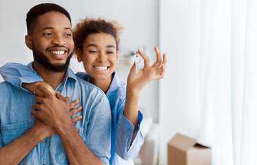 Joyful African American Couple Holding Key Embracing Standing In New Flat After Moving. Selective Focus, Copy Space