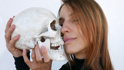 Close-up of a cute young woman holding a skull to her face