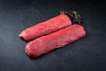 Raw lamb salmon fillet offered as close-up on a rustic black board with dried cranberries and herbs...