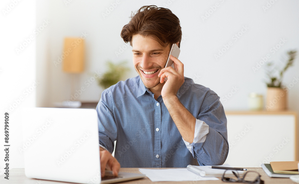 Aufkleber A man is smiling and talking on a phone while working on a laptop. He is seated at a desk and has paperwork in front of him.