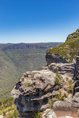 Walls Lookout, a panoramic view of the Blue Mountains National Park in New South Wales, Australia, featuring a lush valley, rugged cliffs, and a clear blue sky.