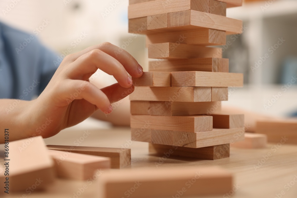 Poster Child playing Jenga at wooden table indoors, closeup