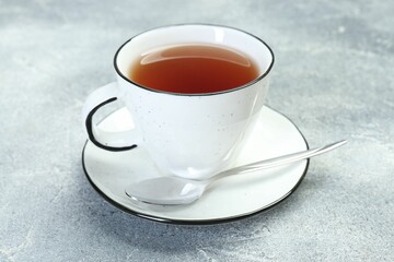 Aromatic tea in cup and spoon on grey table