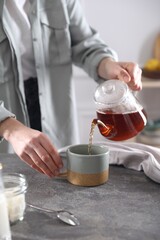 Woman pouring hot tea into cup at grey table, closeup