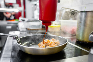 Close-up of shrimp being cooked in a frying pan with sauce poured from a squeeze bottle
